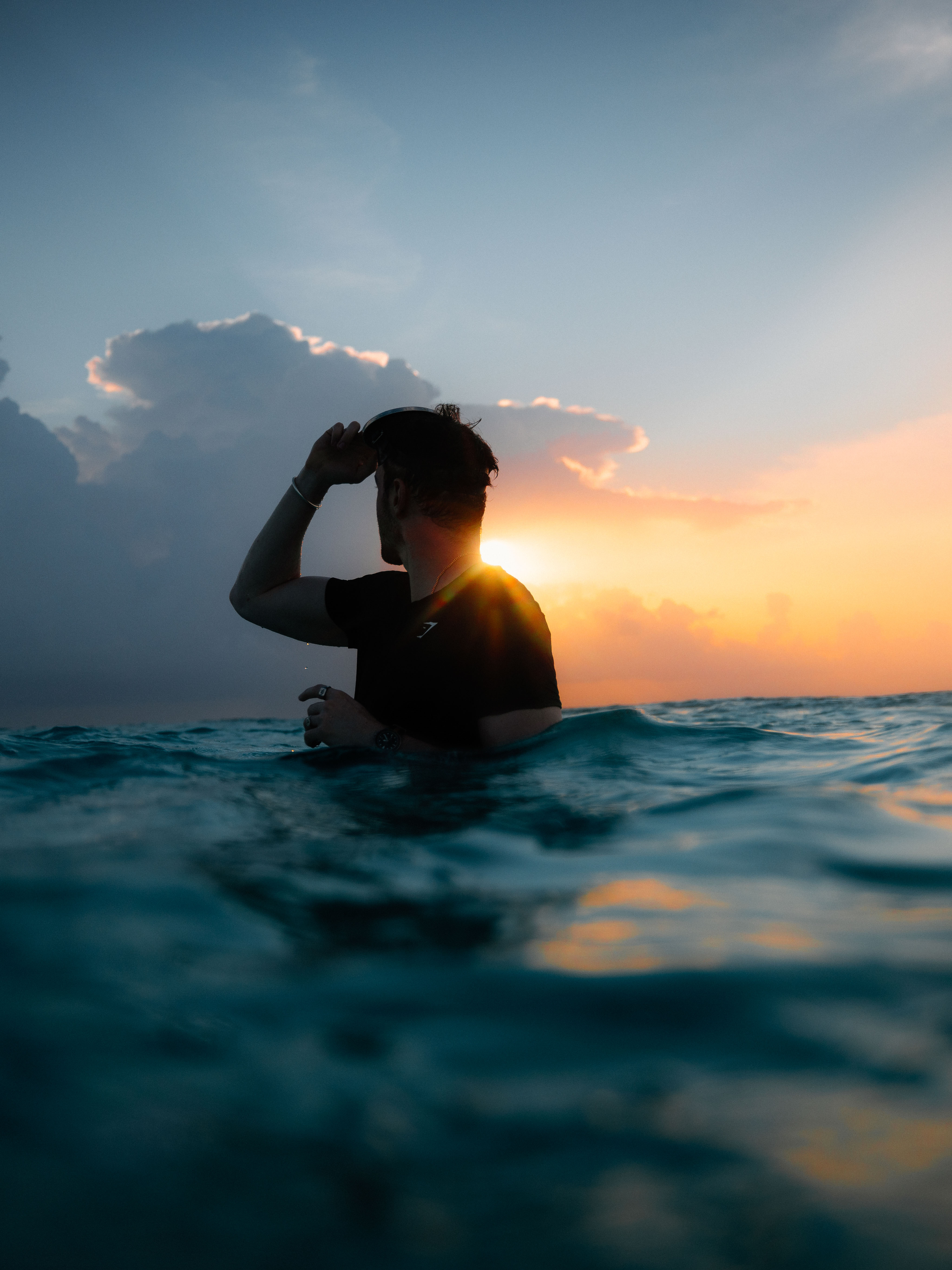A man standing waist deep in the ocean at sunset